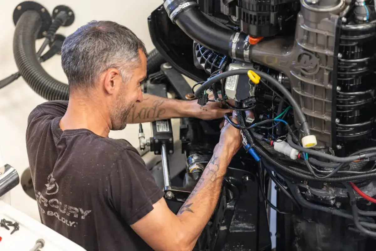 Un mécanicien travaille sur un moteur hors-bord complexe. Il vérifie les connexions, espérant qu'un moteur serré puisse démarrer après sa révision.