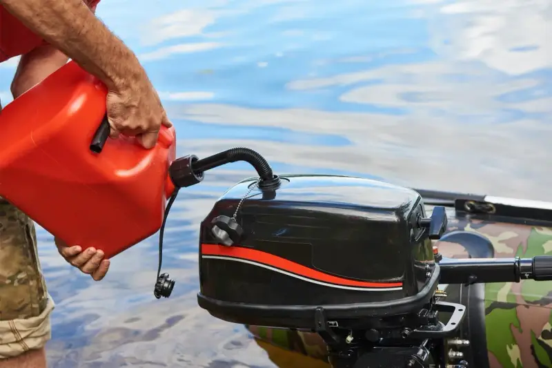 Un homme verse de l'essence dans un moteur hors-bord. Il se demande quel essence pour moteur 2 temps utiliser pour sa sortie en bateau.